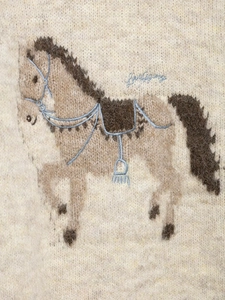 Detailed close-up of horse jacquard pattern and blue embroidery on white wool knit sweater