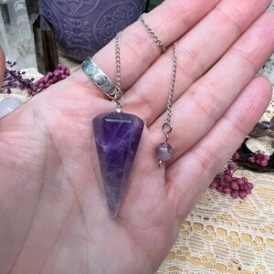 Handheld amethyst pendulum necklace with a faceted hexagonal crystal and silver chain