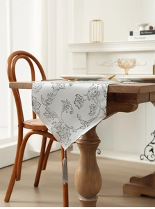 Close-up of silver-gray Christmas table runner with black floral jacquard and tassels
