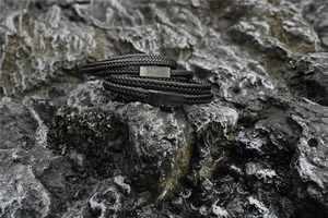 Detail von geflochtenen schwarzen Lederarmbändern mit Magnetverschluss auf rauem Felsboden