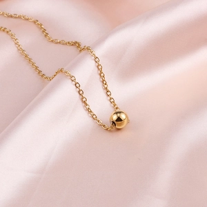 Detail of 18K gold-plated bead pendant on a fine link chain over soft pink silk fabric