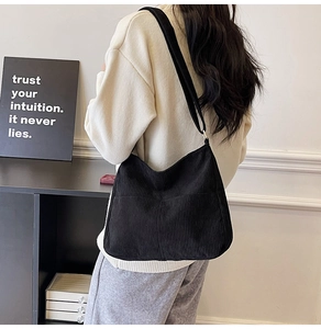 Detail showing a black corduroy tote bag worn by a model in a minimalist setting