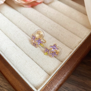 Detail of purple lilac flower clip-on earrings with gold finish on a beige velvet tray