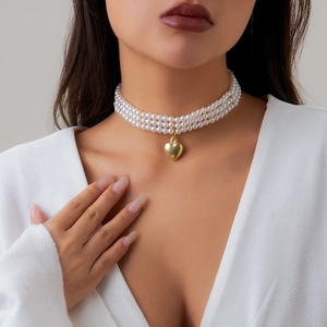 Close-up of triple-layer pearl choker necklace with a gold heart pendant on model