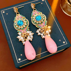 Détails de boucles d'oreilles dorées avec pierres bleues, perles et gouttes roses