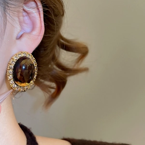 Close-up of vintage oval resin earring with amber stone and gold setting on model