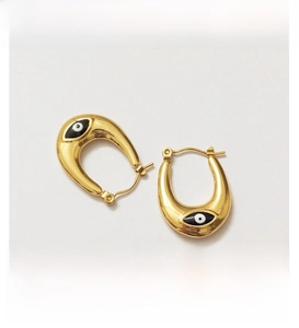 Detail of U-shaped gold earrings featuring black and white evil eye enamel drops