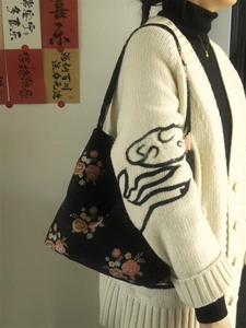 Floral embroidery detail on a vintage black shoulder bag styled with a white cardigan