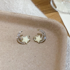 Macro view of gold star and moon stud earrings with sparkling crystals and cream glaze