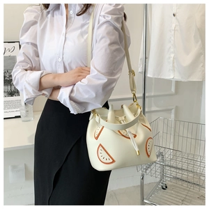 Detail of white drawstring bucket bag featuring orange fruit slice patterns and gold hardware