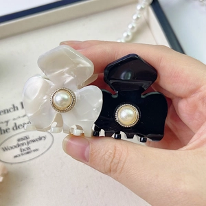 Detail of small flower-shaped hair clips with pearls in black and marble white acetate