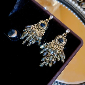 Close-up of vintage gold earrings with navy stones and dark grey crystal tassels in a box