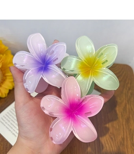 Detail of three gradient candy-colored frangipani hair claws in purple, green, and pink
