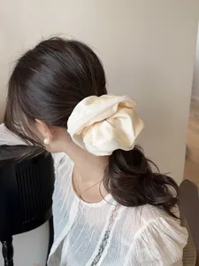 Detail of oversized satin scrunchie in beige silk-like fabric on low ponytail
