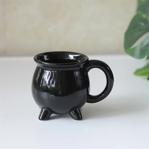 Close-up of a glossy black ceramic witch cauldron mug with tripod feet for Halloween