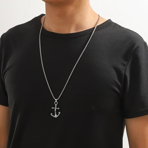 Détail d'un collier avec pendentif ancre et croix en argent porté par un homme