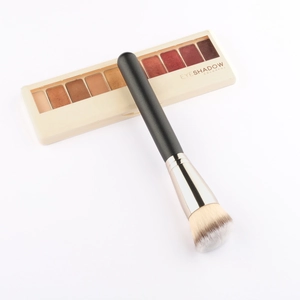 Λεπτομέρεια flat lay από γωνιακό πινέλο foundation δίπλα σε μια παλέτα σκιών ματιών 9 χρωμάτων