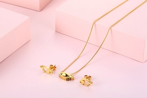 Golden eye-shaped jewelry set with necklace and earrings on pink geometric display