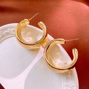 Close-up of chunky gold C-shaped hoop earrings on a white tray with silk backdrop