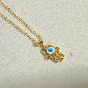 Detailed close-up of golden Hamsa Hand pendant featuring a blue Evil Eye and zircon accents
