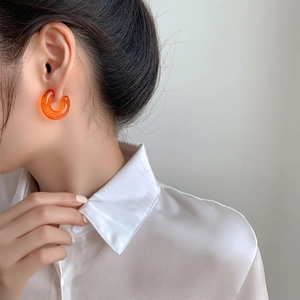 Detail view of a model wearing orange jelly-colored C-shaped acrylic resin hoop earrings