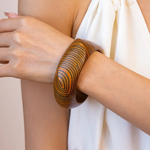 Detailed macro shot of a wide wooden bangle with orange and black concentric oval patterns