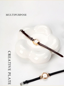 Close-up of vintage square gold watch on a white flower-shaped ceramic jewelry tray