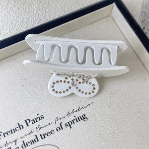 Detailed macro shot of a white acetic acid hair claw clip with rhinestones and bow design