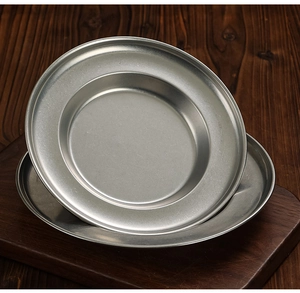 Close-up of stacked vintage-style stainless steel soup plates on a rustic wooden board