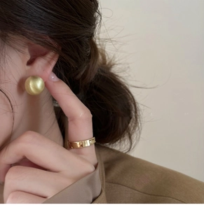 Close-up of elegant gold brushed round stud earrings and a wide band ring on a model