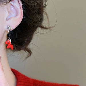 Detail of red pony and star stud earrings worn by a model in a cozy red sweater