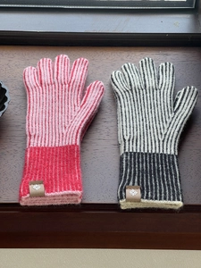 Detalle de guantes de punto a rayas rojo-rosa y negro-gris con logo de cuero sobre madera