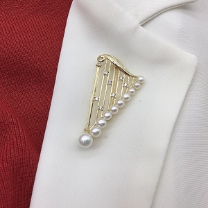Detail of harp-shaped gold brooch with white pearls and small diamonds on white blazer lapel