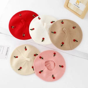 Close-up of knit beret hats in multiple colors featuring delicate cherry embroidery