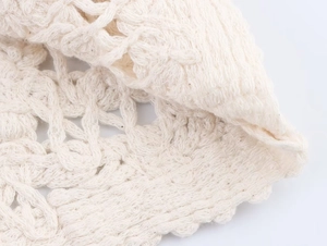 Macro view of ivory crochet knit fabric showing intricate hollow-out texture and soft cotton yarn