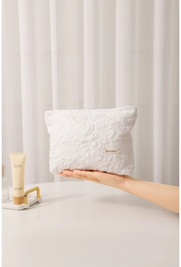 Detail of white embossed floral fabric makeup bag with a minimalist brand label tag