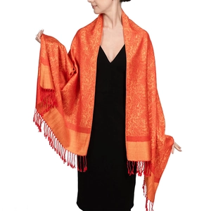 Close-up of orange jacquard scarf with intricate patterns and fringe on a black dress