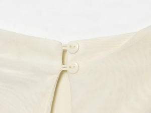 Detail of cream mesh dress featuring double button closure and delicate fabric texture