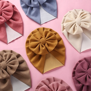 Flat lay of soft baby beanies featuring oversized bows in various earthy and pastel colors