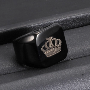 Close-up of black square stainless steel ring with crown engraving on leather cushion