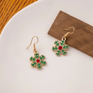 Close-up of green snowflake earrings with red crystal center on a white ceramic tray