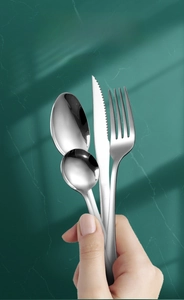 Polished stainless steel cutlery set held by hand against green marble background