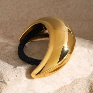 Close-up of minimalist gold curved hair ring on natural sand and stone background