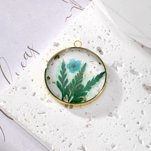Detailed close-up of a gold metal frame pendant with blue dried flowers and gold leaf