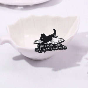 Cute black cat enamel pin with coffee and books theme on a white ceramic leaf bowl