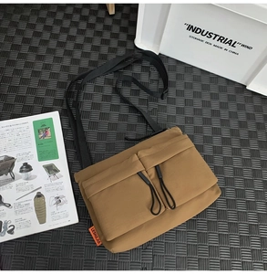 Flat lay of khaki nylon messenger bag with double front pockets on an outdoor camping mat