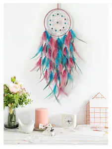 Detail of a handmade dream catcher with pink and blue feathers hanging on a white wall