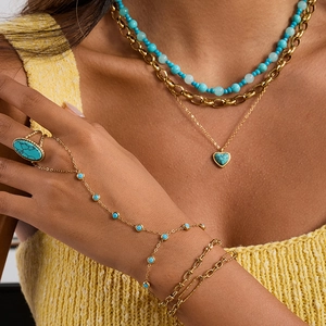 Detailansicht von Türkisschmuck-Set mit Ringen und Halsketten auf gelbem Stricktop
