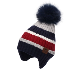 Close-up of winter knit beanie showing fluffy faux fur pompom and leather brand patch