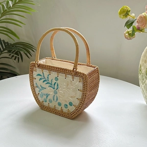 Detail of hand-woven rattan shell bag with white leather patch and blue floral pattern